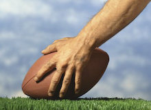Football and Cheerleading Risks // Center's hand on ball (Getty Images/Brand X)